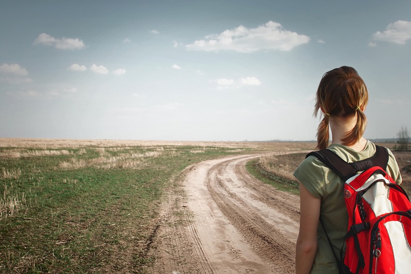 Young woman with backpack on rural road looking to somewhere